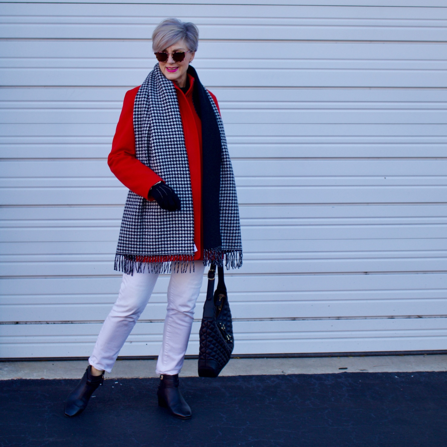 beth from Style at a Certain Age wears a red stadium coat, houndstooth cashmere scarf, white denim, striped cashmere crewneck, black ankle boots and quilted hobo handbag