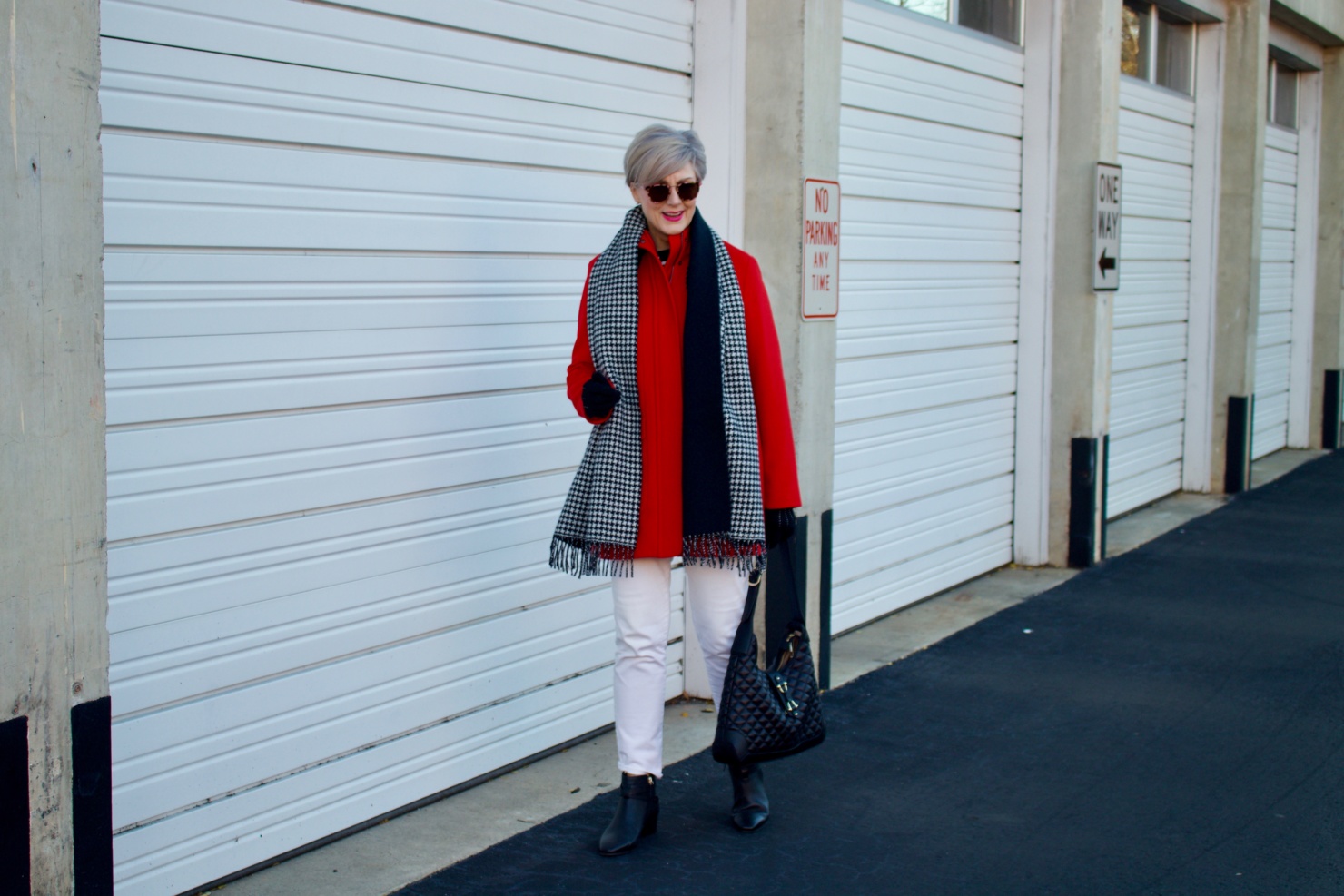 beth from Style at a Certain Age wears a red stadium coat, houndstooth cashmere scarf, white denim, striped cashmere crewneck, black ankle boots and quilted hobo handbag