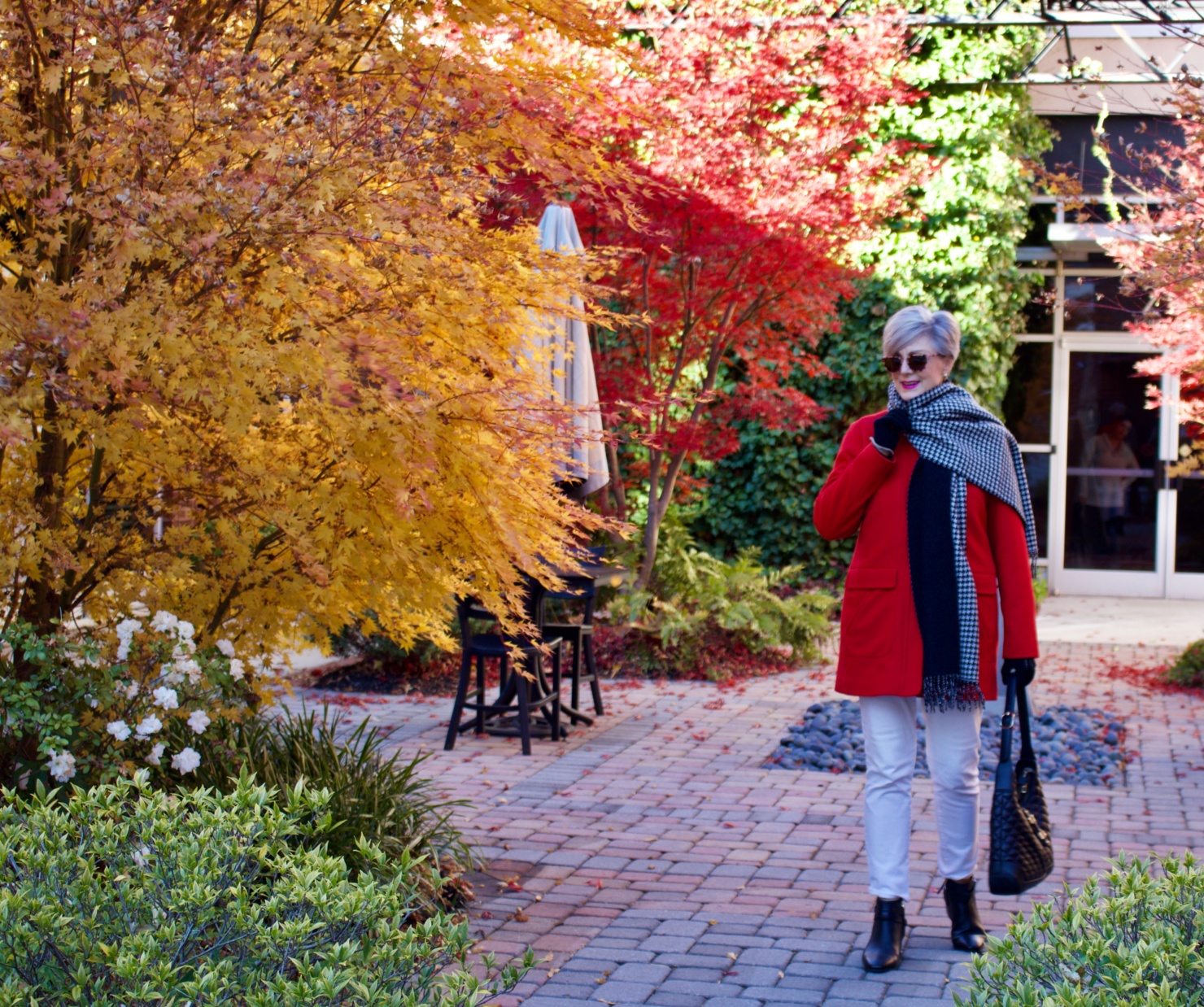 beth from Style at a Certain Age wears a red stadium coat, houndstooth cashmere scarf, white denim, striped cashmere crewneck, black ankle boots and quilted hobo handbag