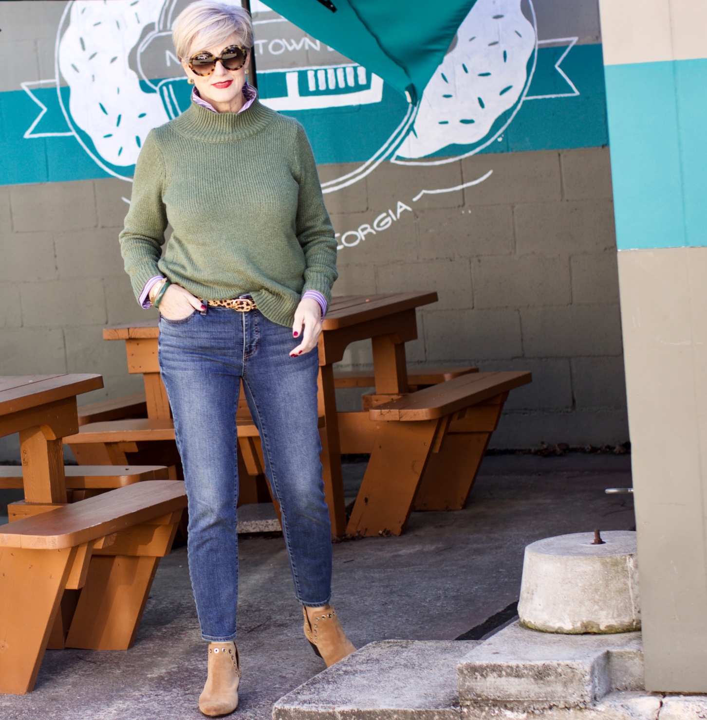 beth from Style at a Certain Age wears a chunky turtleneck layered over a stripe button down, skinny ankle jeans, a denim jacket, and booties