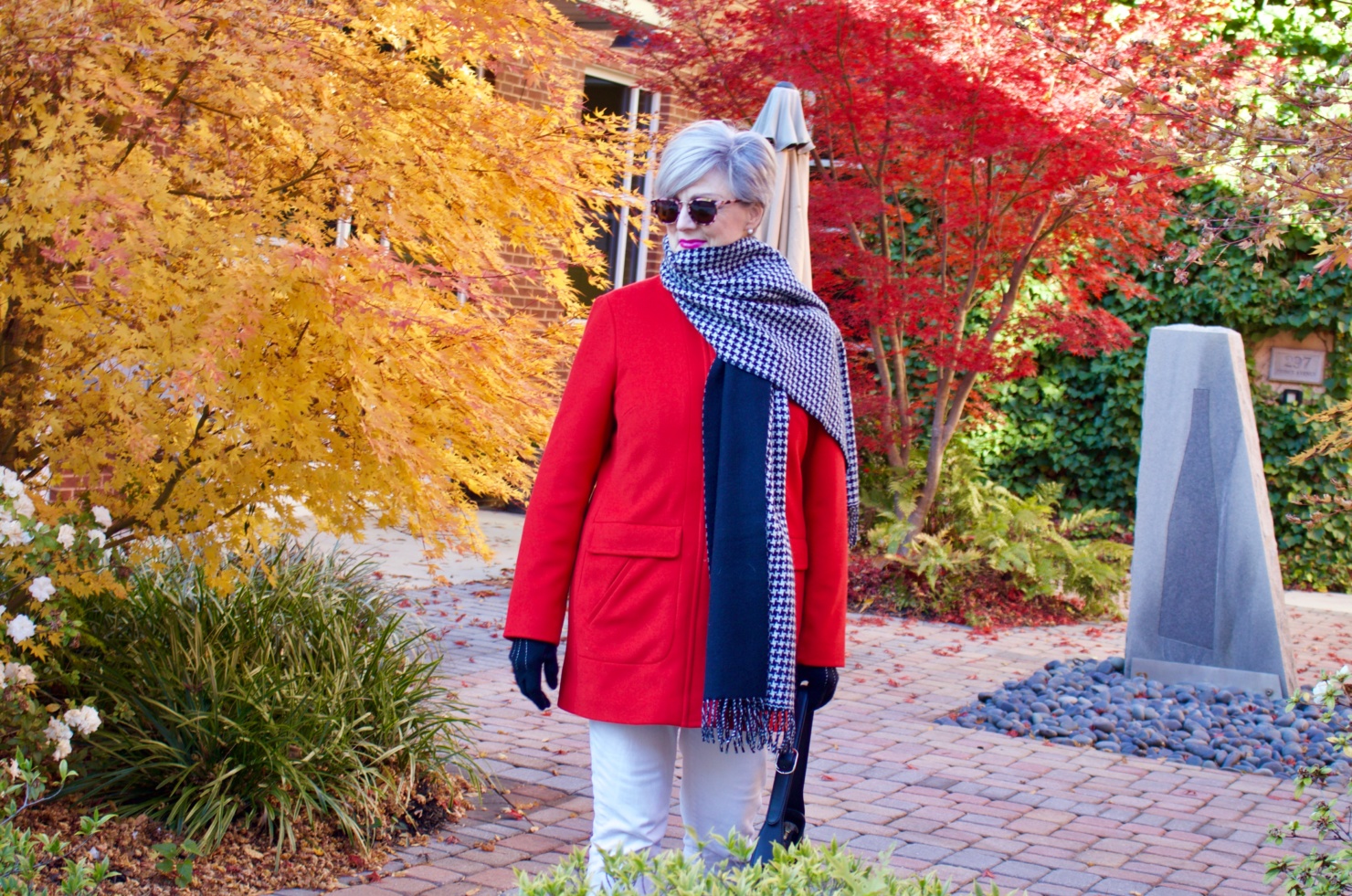 beth from Style at a Certain Age wears a red stadium coat, houndstooth cashmere scarf, white denim, striped cashmere crewneck, black ankle boots and quilted hobo handbag