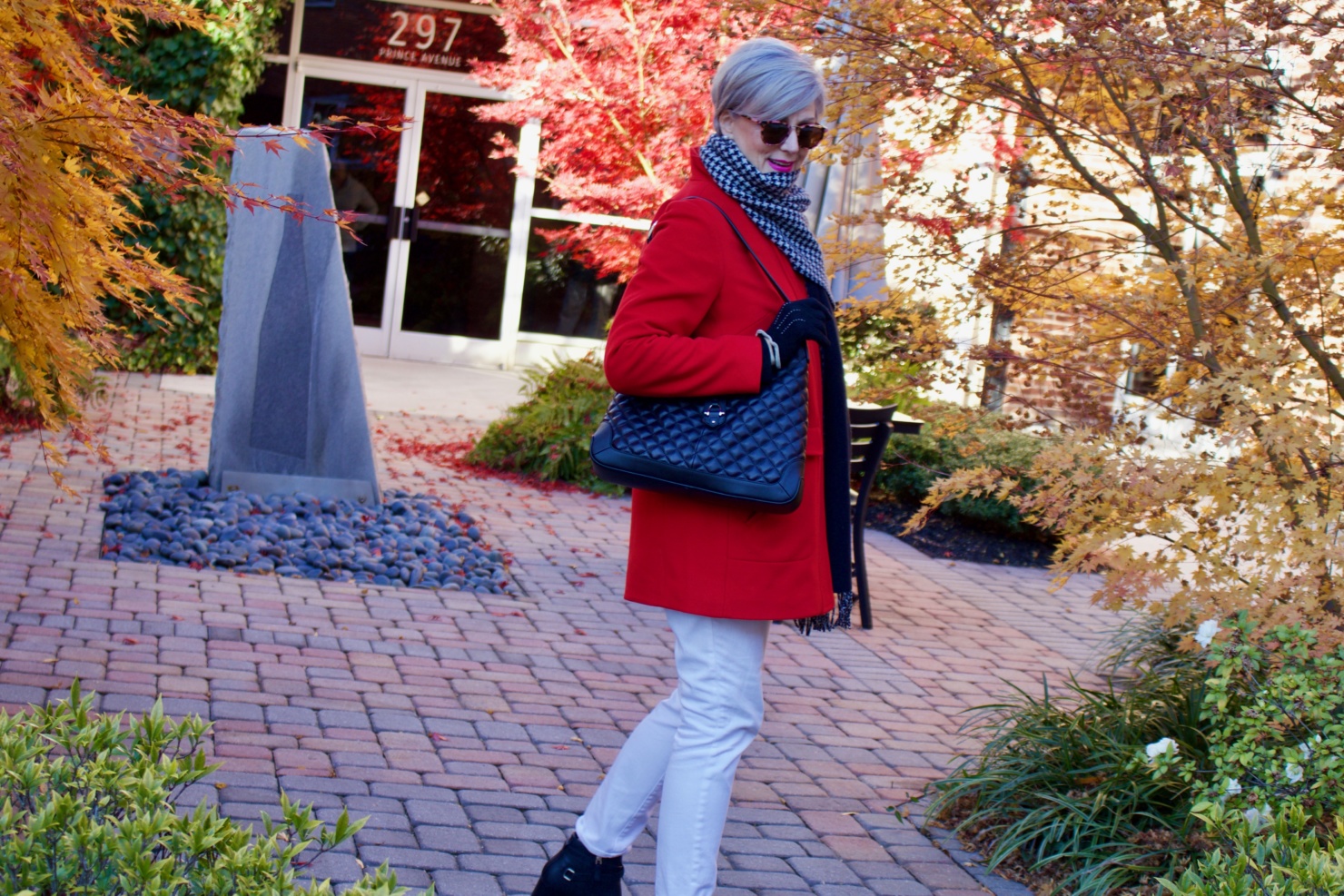 beth from Style at a Certain Age wears a red stadium coat, houndstooth cashmere scarf, white denim, striped cashmere crewneck, black ankle boots and quilted hobo handbag