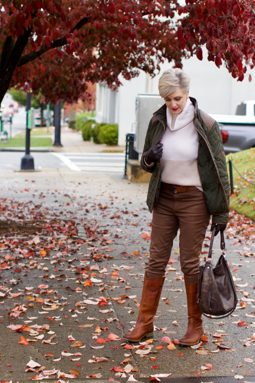 beth from Style at a Certain Age is wearing Ralph Lauren faux leather pants, chunky cashmere sweater, green utility jacket, Frye boots, and Frye hobo handbag