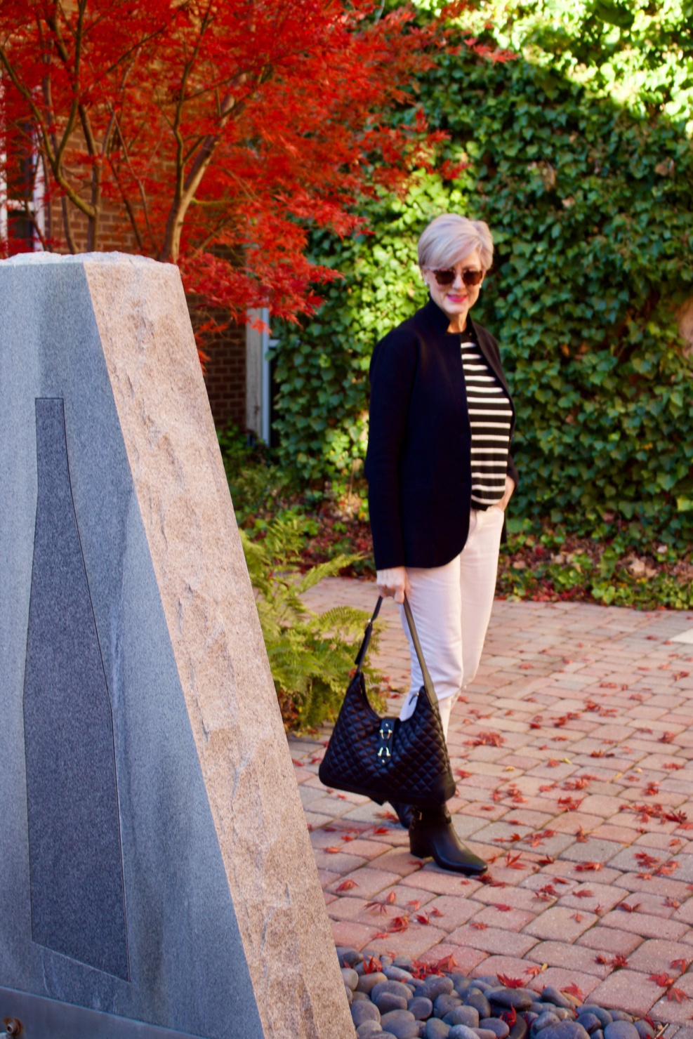 beth from Style at a Certain Age wears a red stadium coat, houndstooth cashmere scarf, white denim, striped cashmere crewneck, black ankle boots and quilted hobo handbag