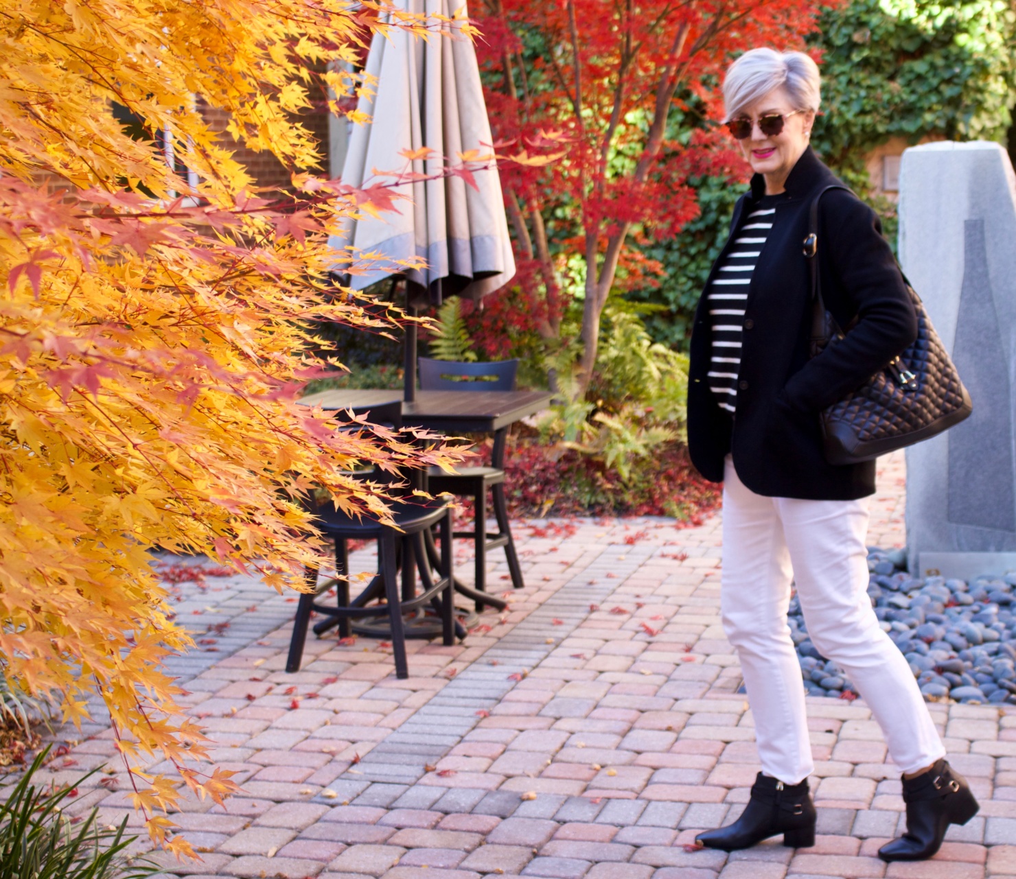 beth from Style at a Certain Age wears a red stadium coat, houndstooth cashmere scarf, white denim, striped cashmere crewneck, black ankle boots and quilted hobo handbag