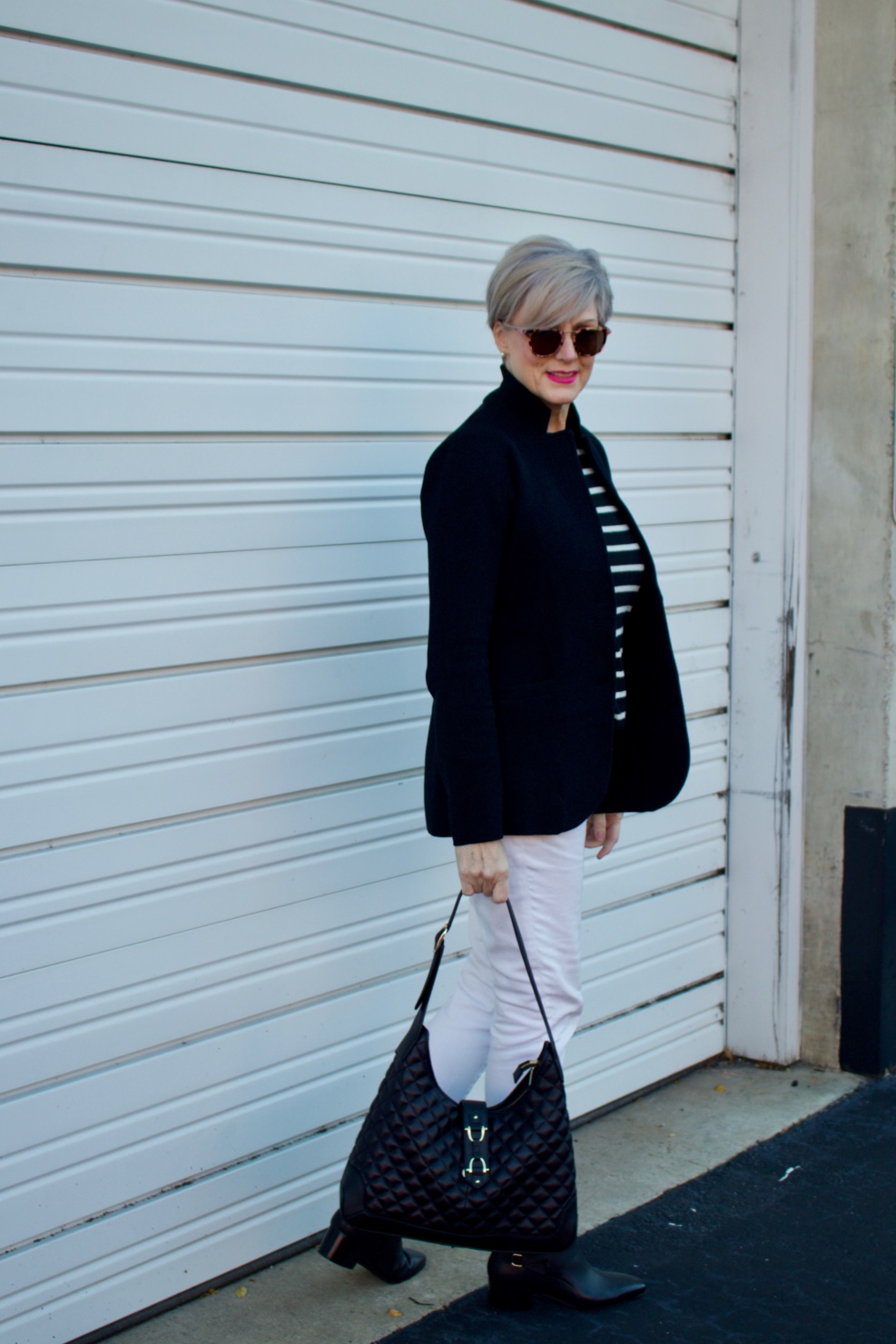 beth from Style at a Certain Age wears a red stadium coat, houndstooth cashmere scarf, white denim, striped cashmere crewneck, black ankle boots and quilted hobo handbag