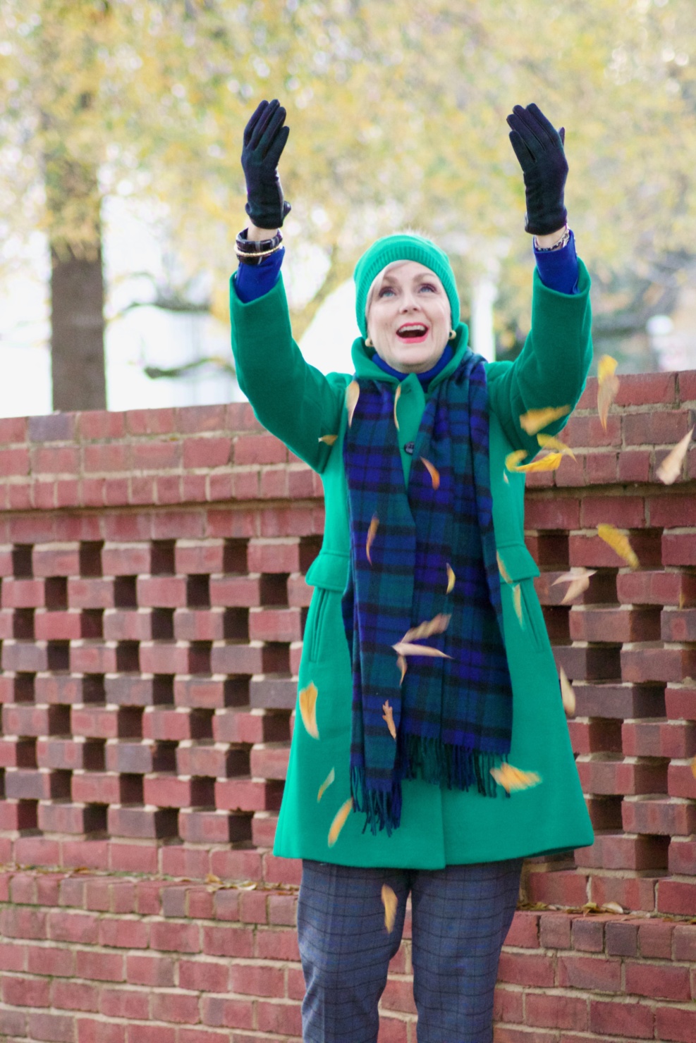 beth from style at a certain age wears plaid pants, cobalt blue turtleneck, green wool coat, blackwatch plaid cashmere scarf, and green beanie