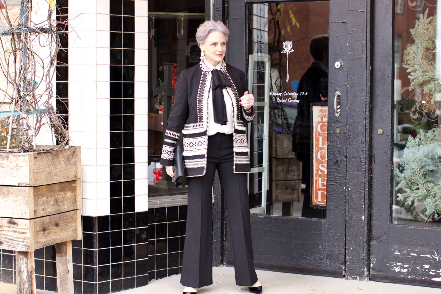 beth from Style at a Certain Age wears black flare pants, bow blouse, embroidered wonderland jacket, and black patent leather pumps