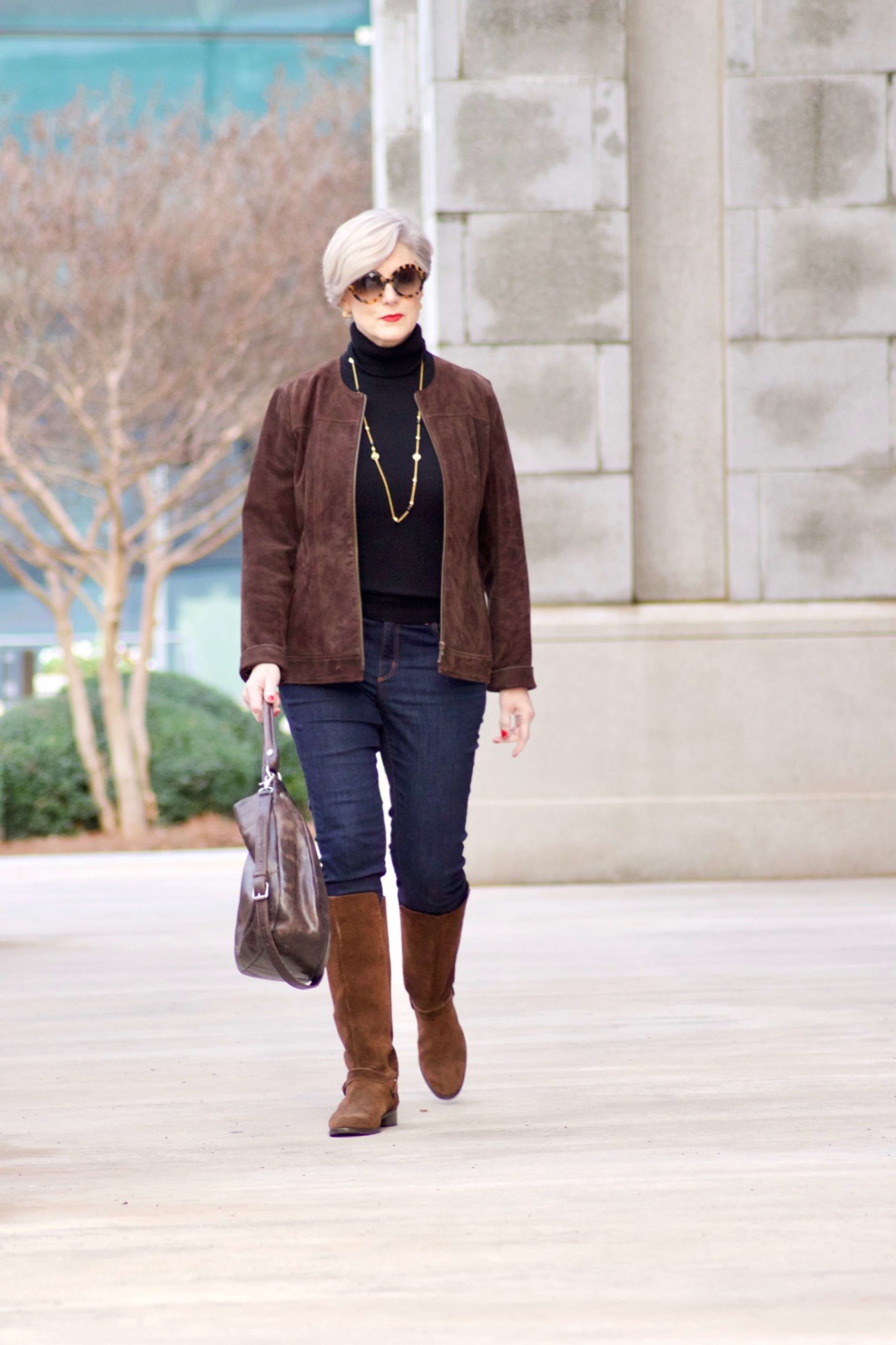 beth from Style at a Certain Age wears a black turtleneck, brown suede jacket, dark rinse denim and suede riding boots