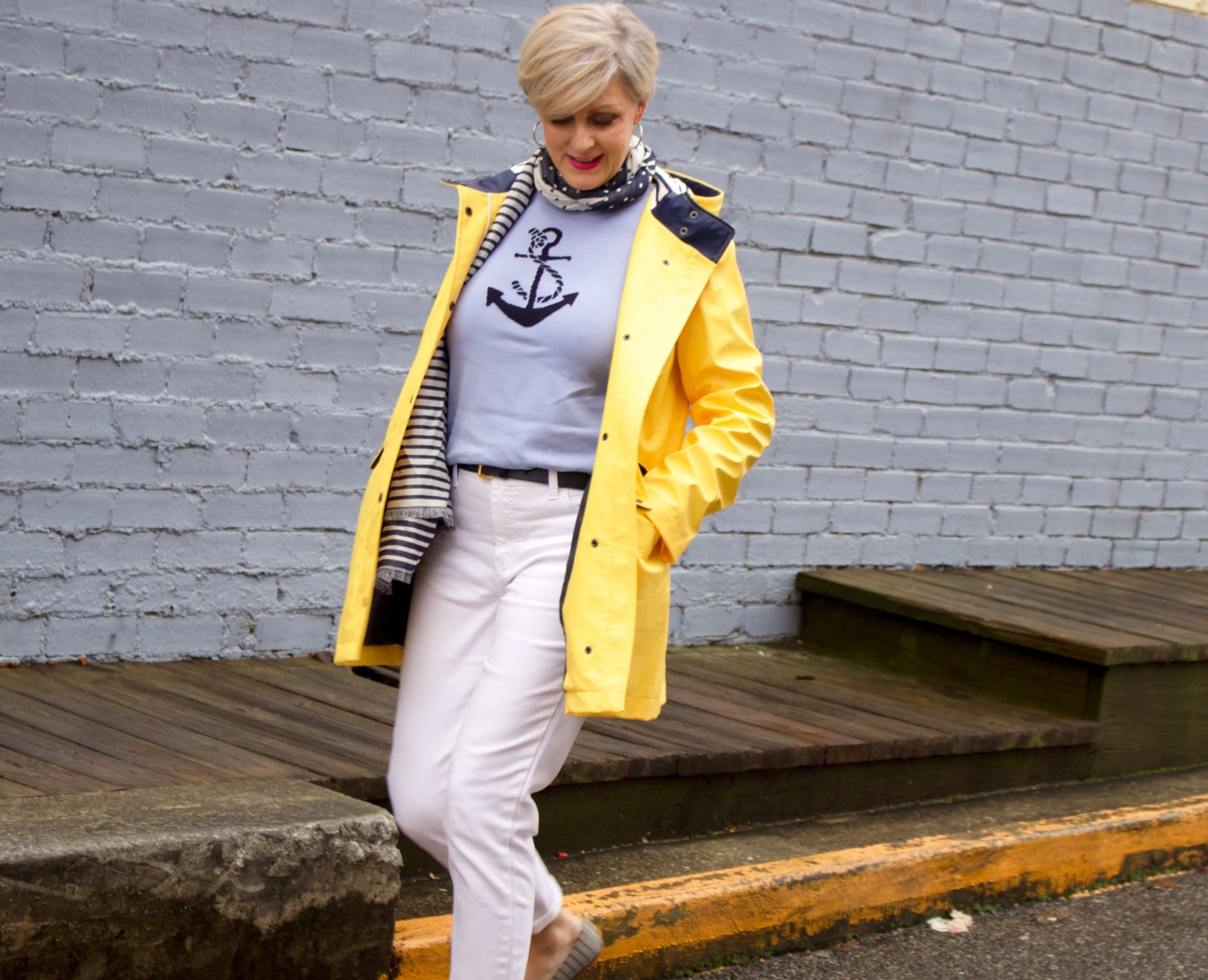 beth from Style at a Certain Age wears a yellow slicker from Talbots, white denim, anchor sweater, polka dot and striped scarf, and striped flats