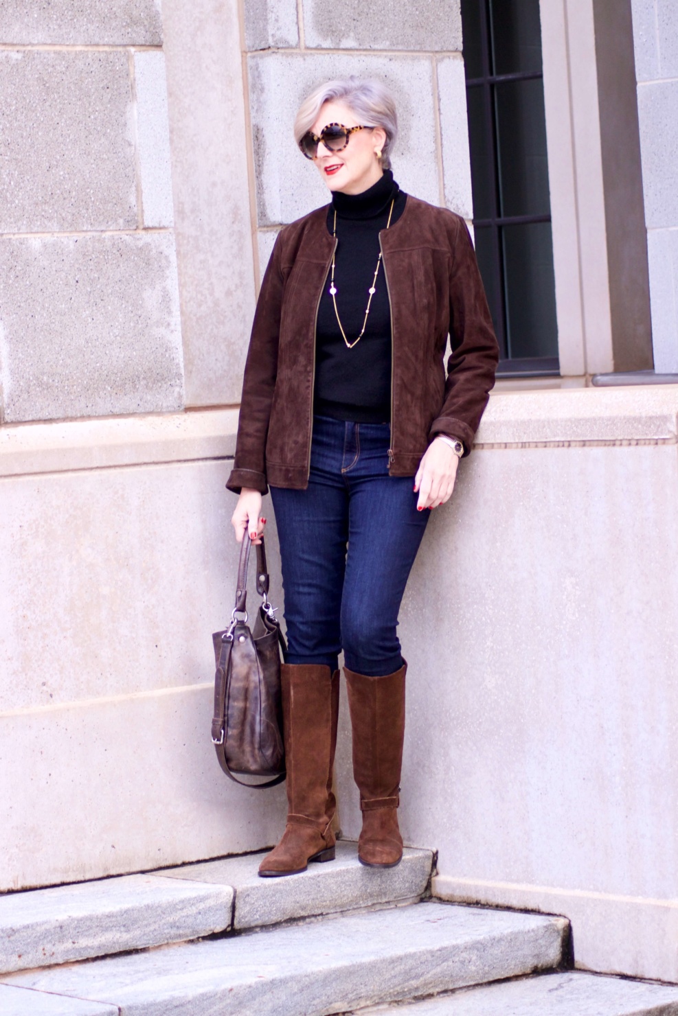 beth from Style at a Certain Age wears a black turtleneck, brown suede jacket, dark rinse denim and suede riding boots