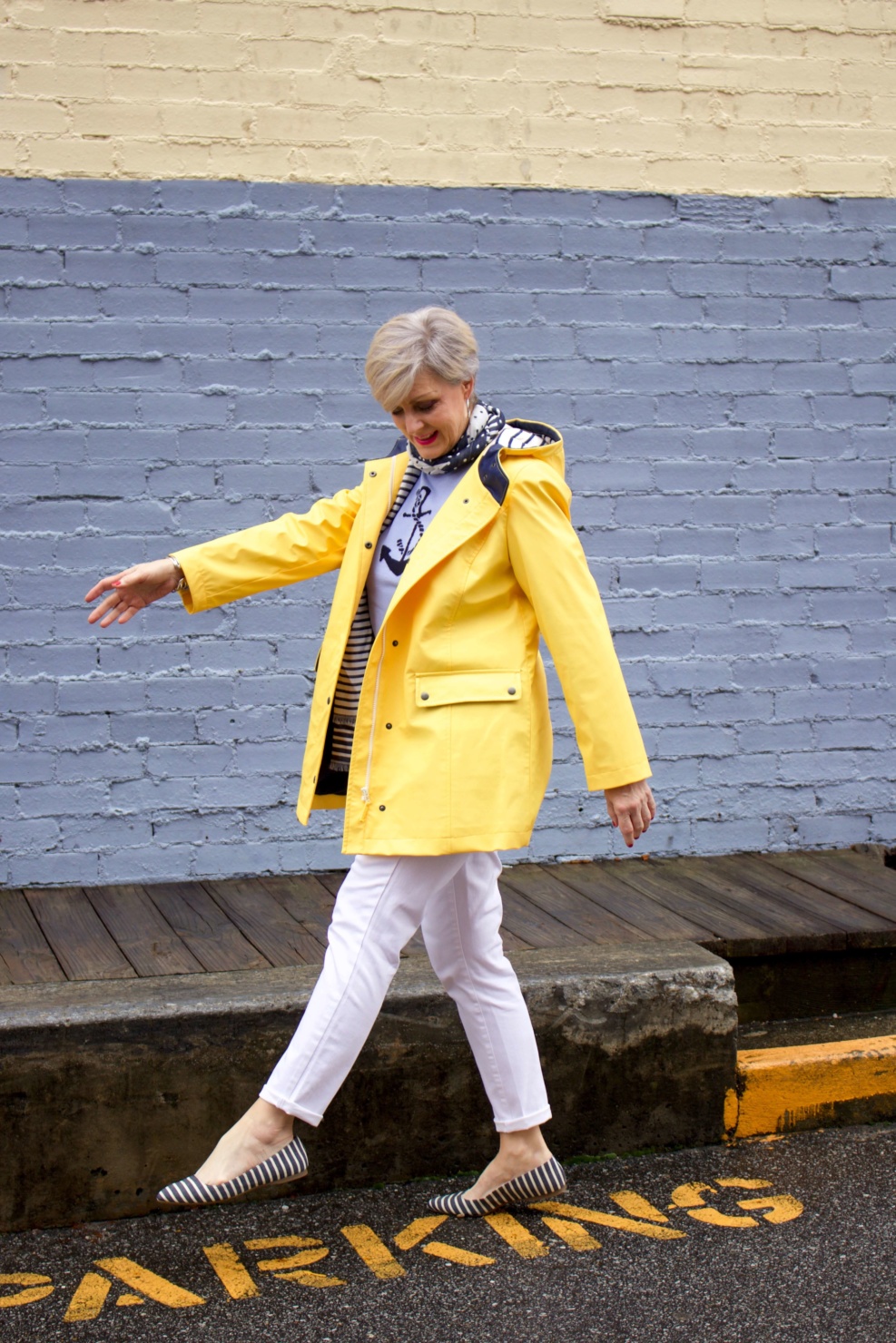 beth from Style at a Certain Age wears a yellow slicker from Talbots, white denim, anchor sweater, polka dot and striped scarf, and striped flats