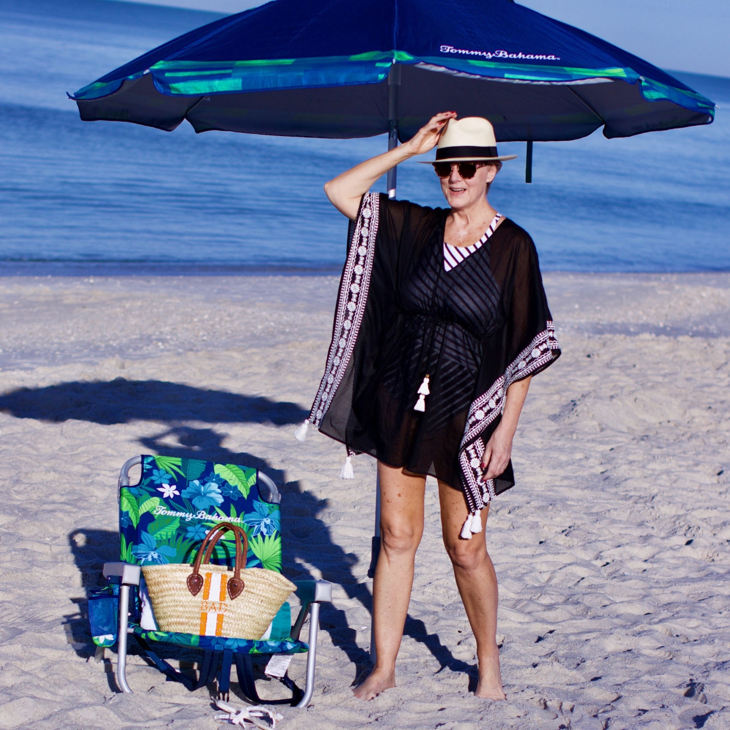 beth from Style at a Certain Age wears beach essentials, Ralph Lauren striped one-piece swimsuit, Tory Burch cover-up, jelly flip-flops, panama hat, and straw tote