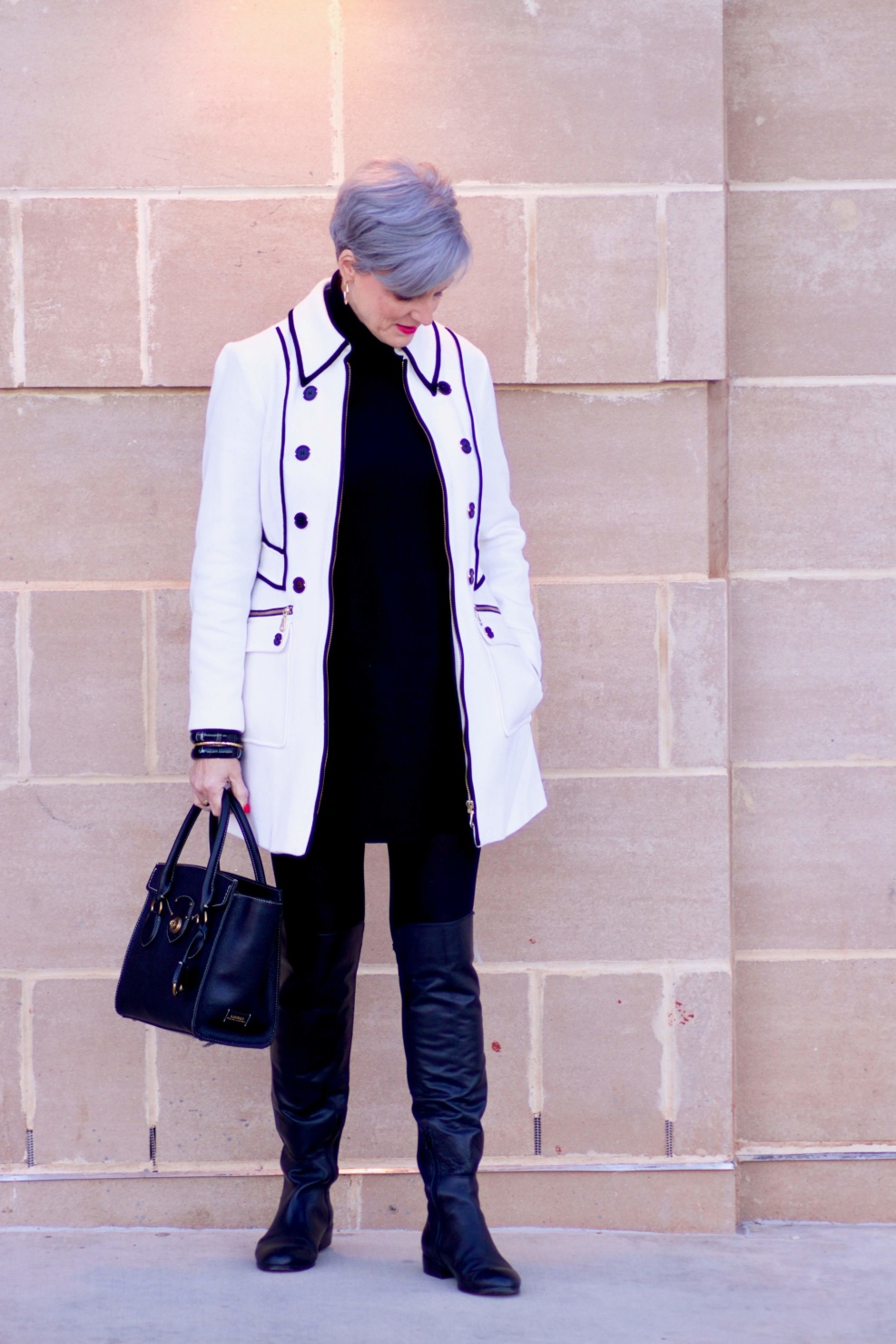 beth from Style at a Certain Age wears a cashmere turtleneck dress, black over the knee boots, and ivory and black coat