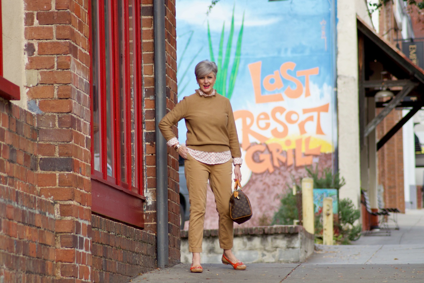 beth from Style at a Certain Age wears a J.Crew camel ruffle neck sweater, slim boy chinos and a Boden modern classic shirt with a bold print.