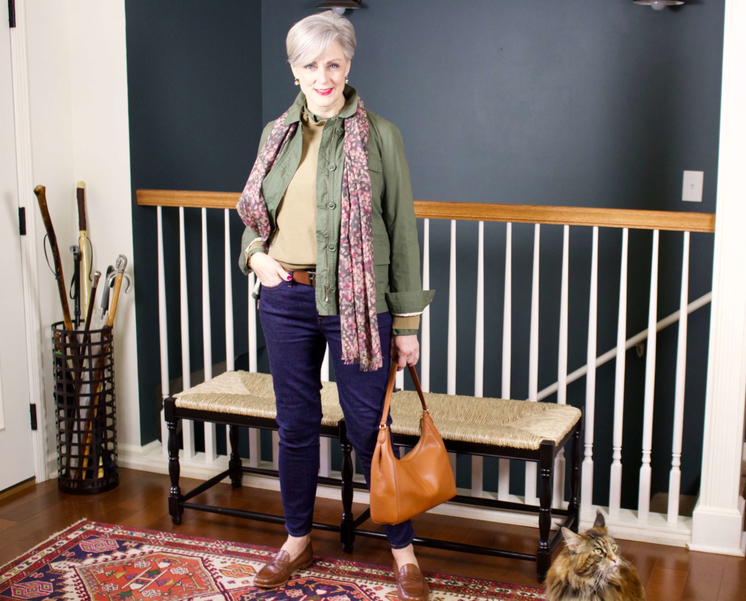 beth from Style at a Certain Age wears a ruffleneck sweater, skinny jeans, green utility jacket, hobo handbag, and loafers