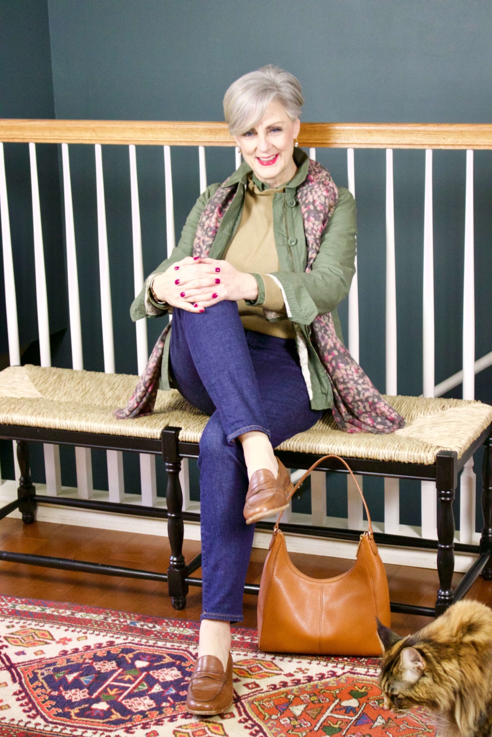 beth from Style at a Certain Age wears a ruffleneck sweater, skinny jeans, green utility jacket, hobo handbag, and loafers