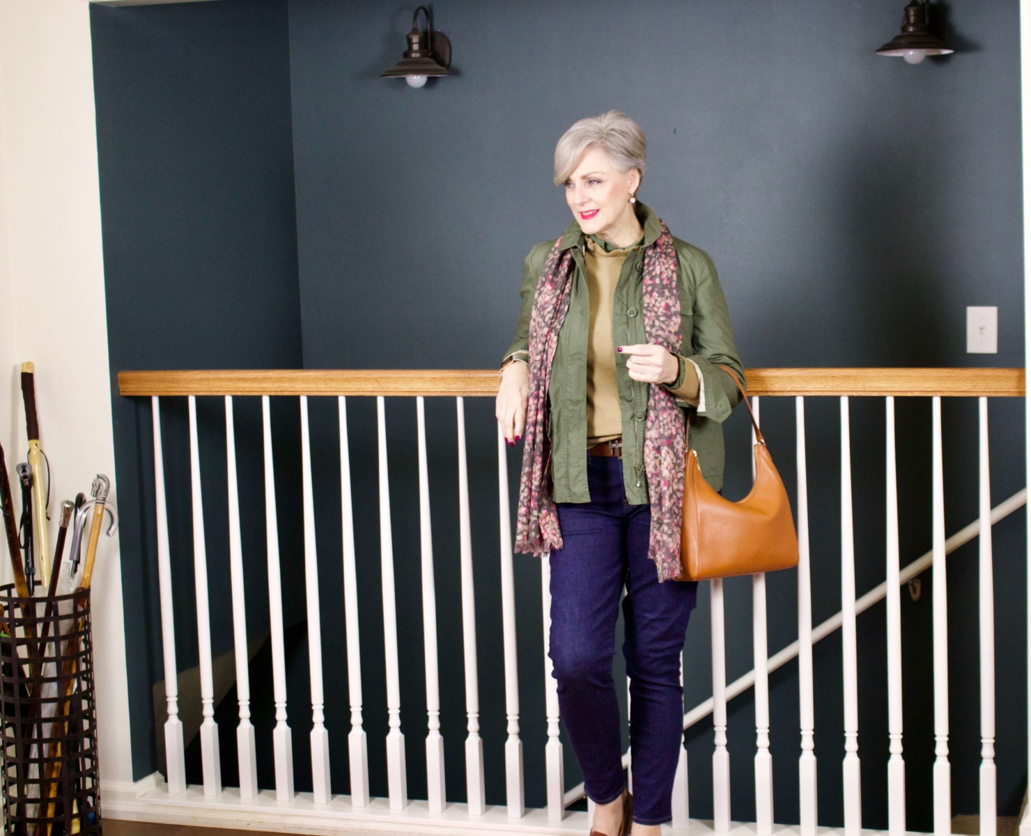 beth from Style at a Certain Age wears a ruffleneck sweater, skinny jeans, green utility jacket, hobo handbag, and loafers