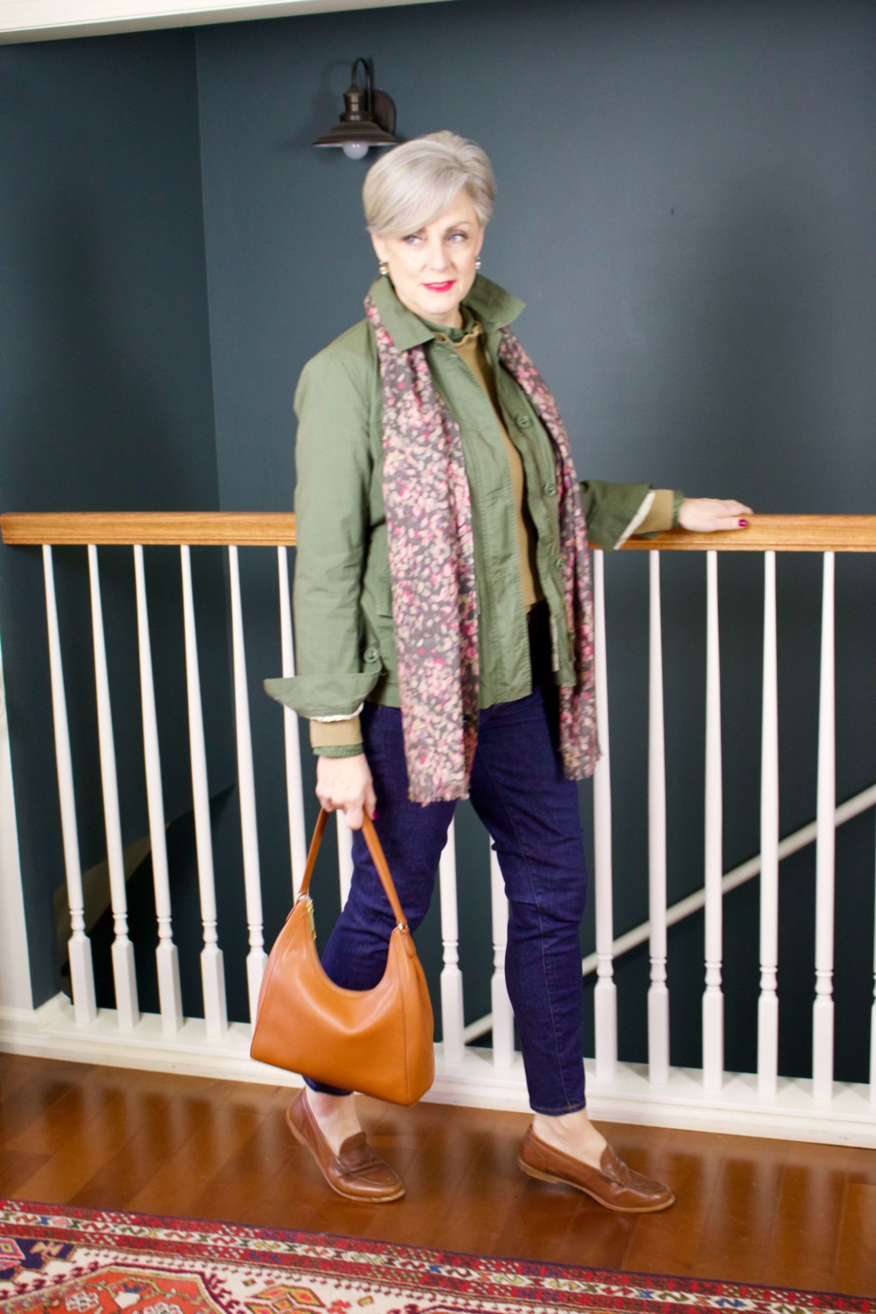 beth from Style at a Certain Age wears a ruffleneck sweater, skinny jeans, green utility jacket, hobo handbag, and loafers