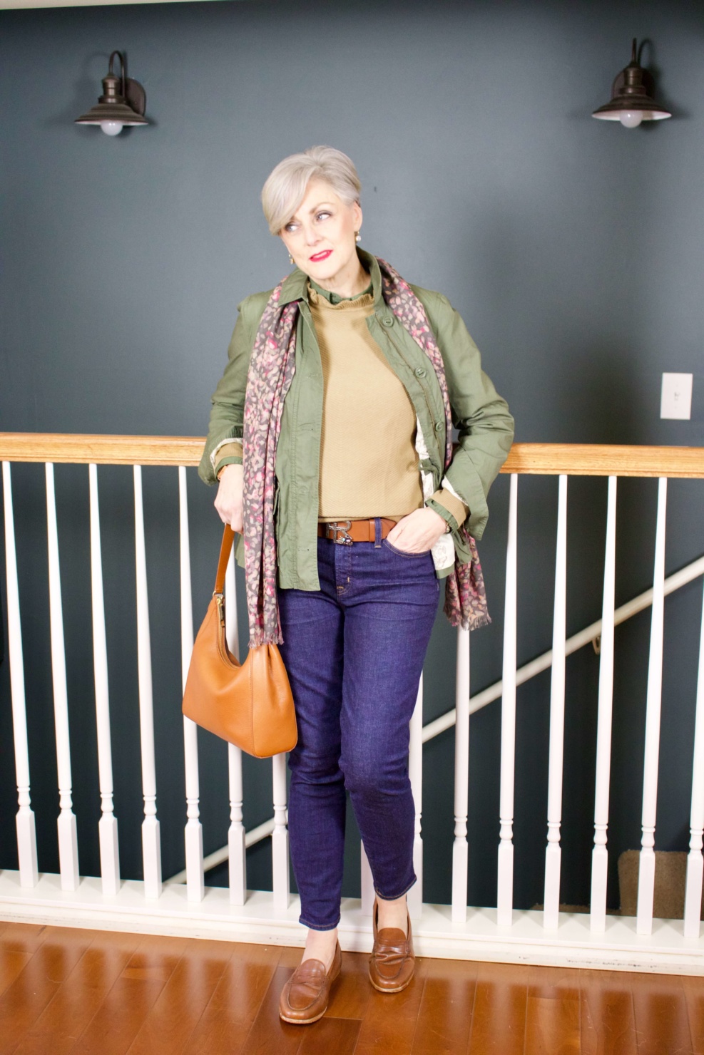 beth from Style at a Certain Age wears a ruffleneck sweater, skinny jeans, green utility jacket, hobo handbag, and loafers