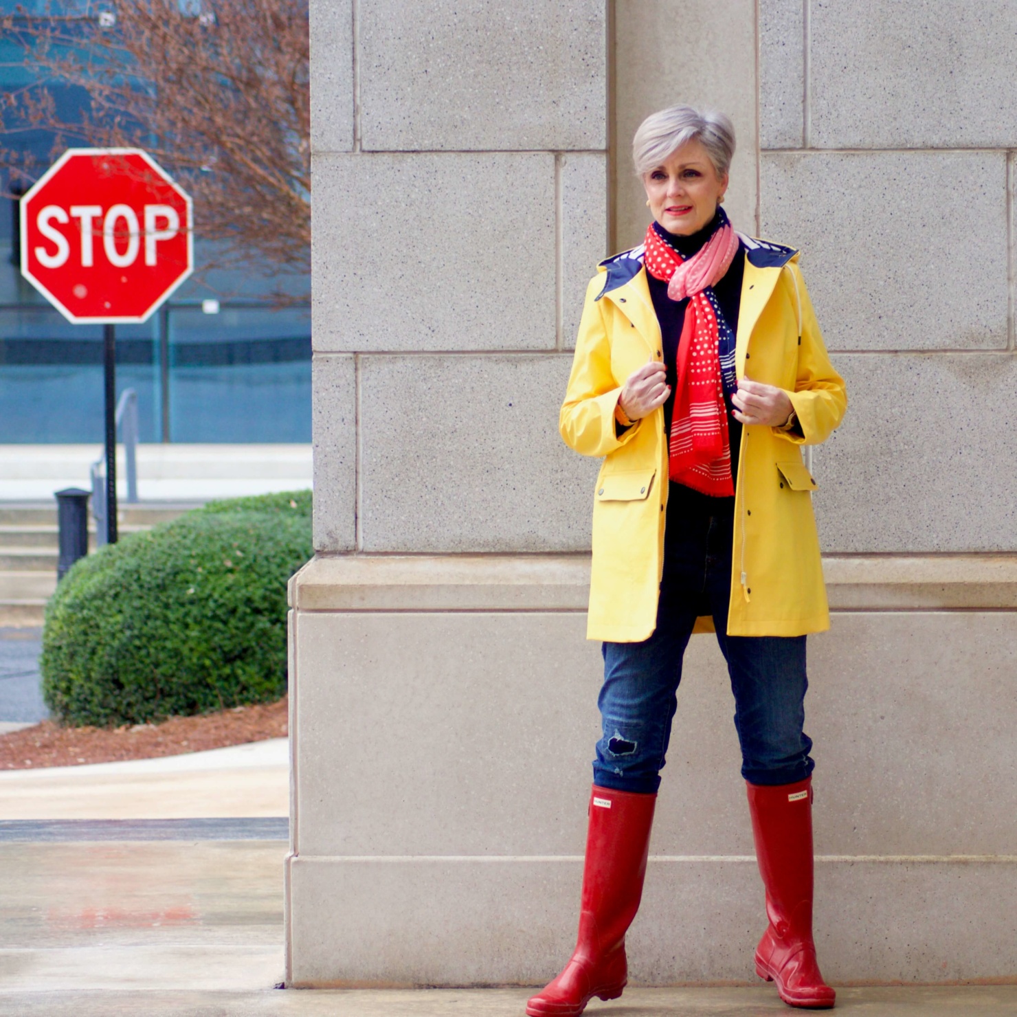 beth from Style at a Certain Age wears Hunter high gloss red rain boots, navy turtleneck, vintage straight jeans, yellow raincoat, and polka dot scarf