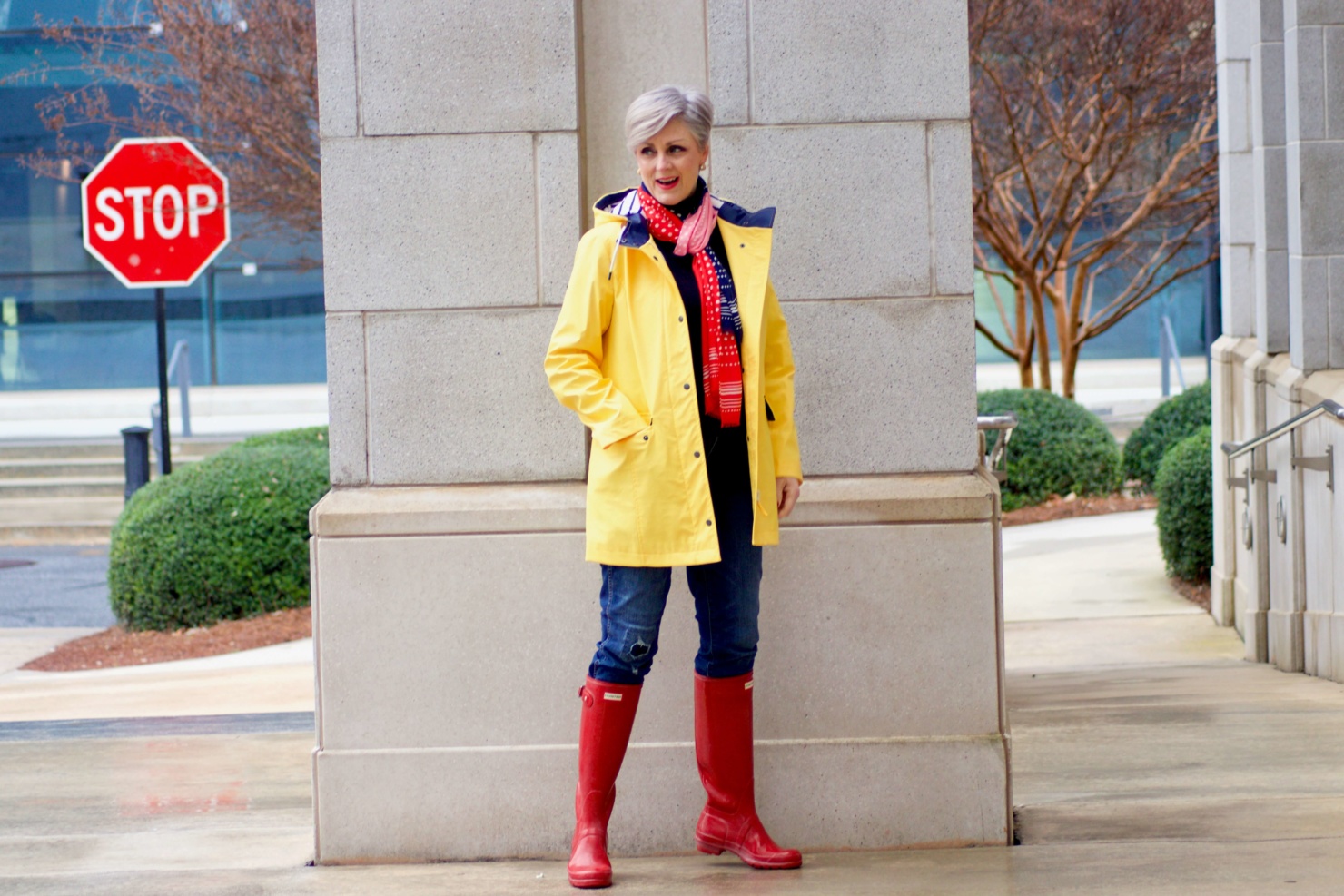 beth from Style at a Certain Age wears Hunter high gloss red rain boots, navy turtleneck, vintage straight jeans, yellow raincoat, and polka dot scarf