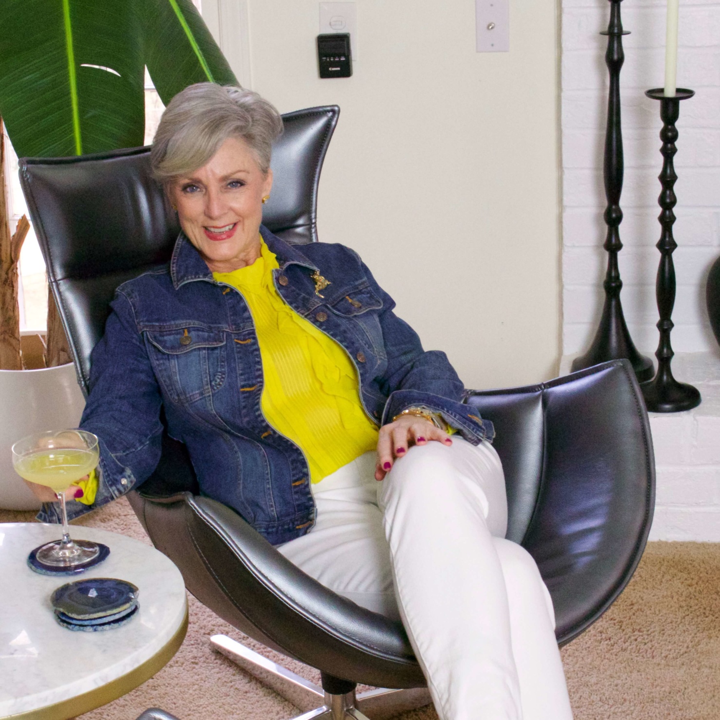 beth from Style at a Certain Age wears a ruffled yellow blouse, white denim, jean jacket, suede driving mocs, and a red camera handbag