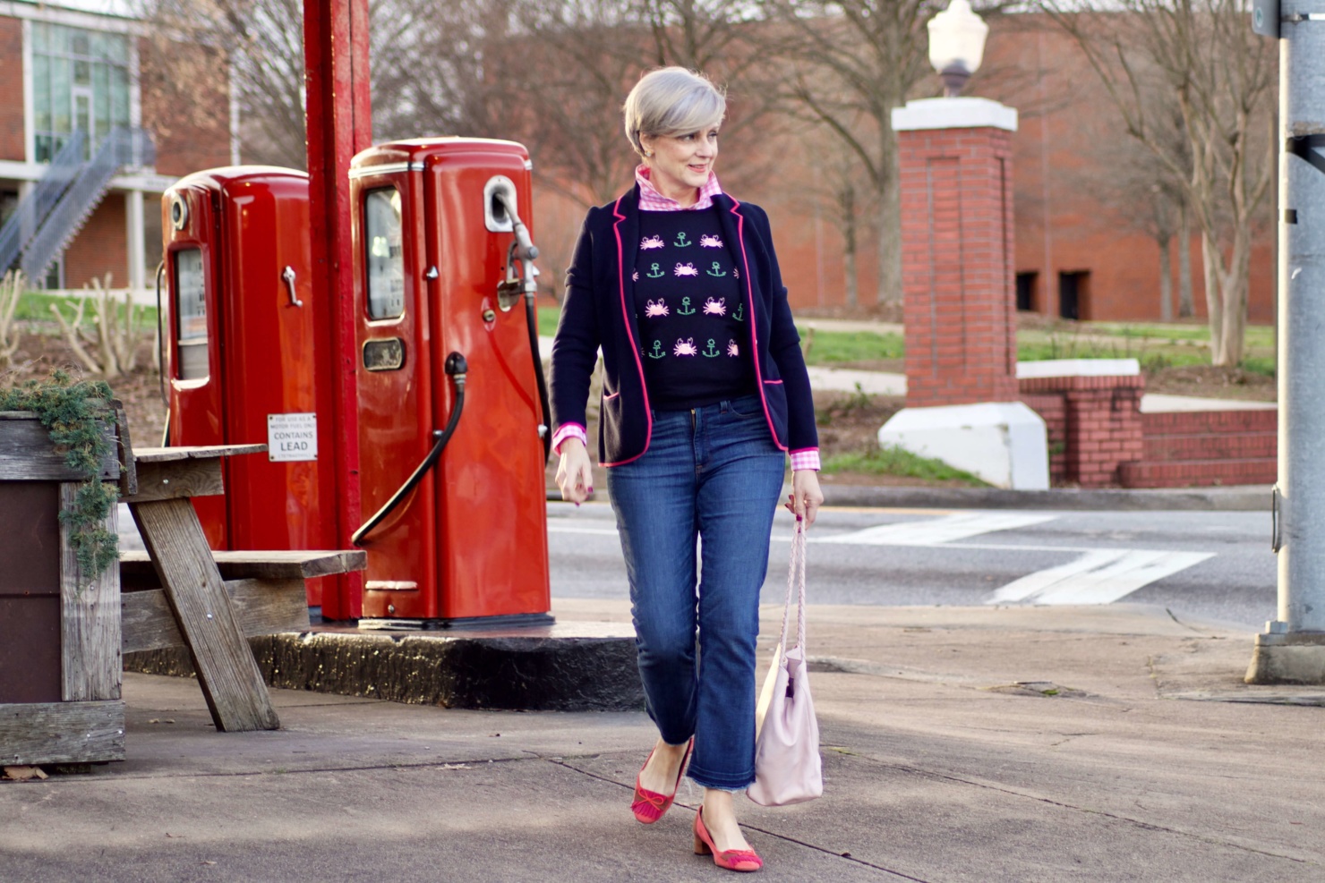 beth from Style at a Certain Age wears a puffer jacket, navy blue knit blazer, novelty sweater, pink gingham check shirt and blue jeans