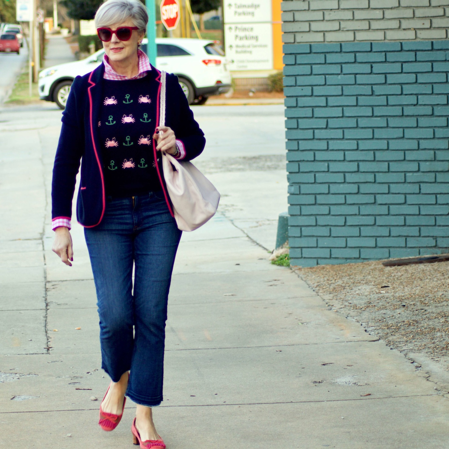 beth from Style at a Certain Age wears a puffer jacket, navy blue knit blazer, novelty sweater, pink gingham check shirt and blue jeans