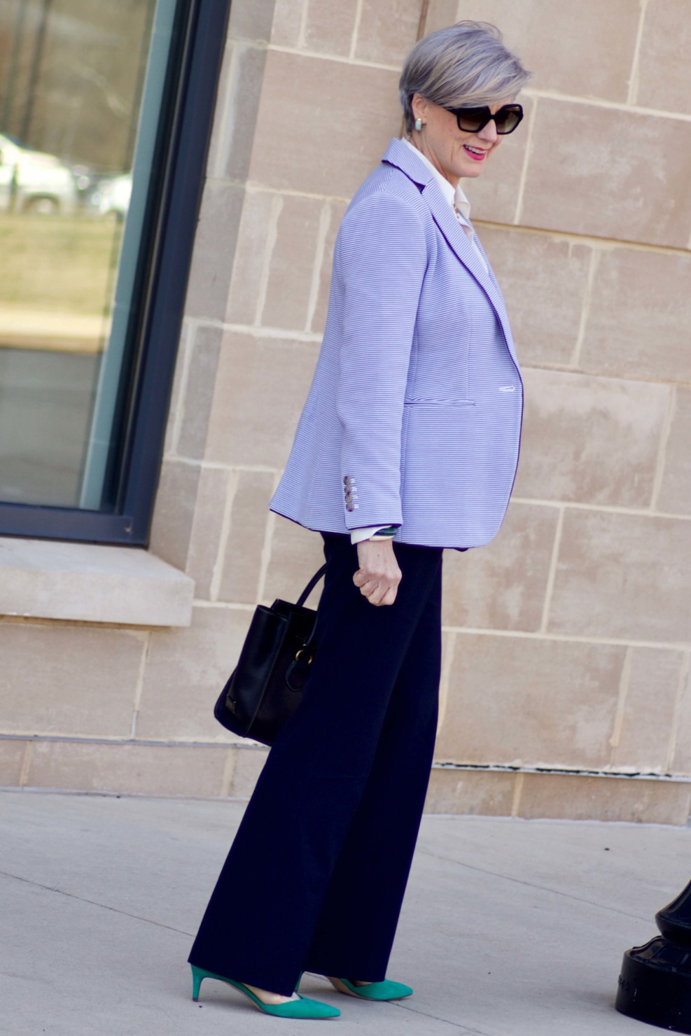 beth from Style at a Certain Age wears a Ann Taylor green trench coat, navy trousers, white essential shirt, knit striped blazer, and green suede pumps.