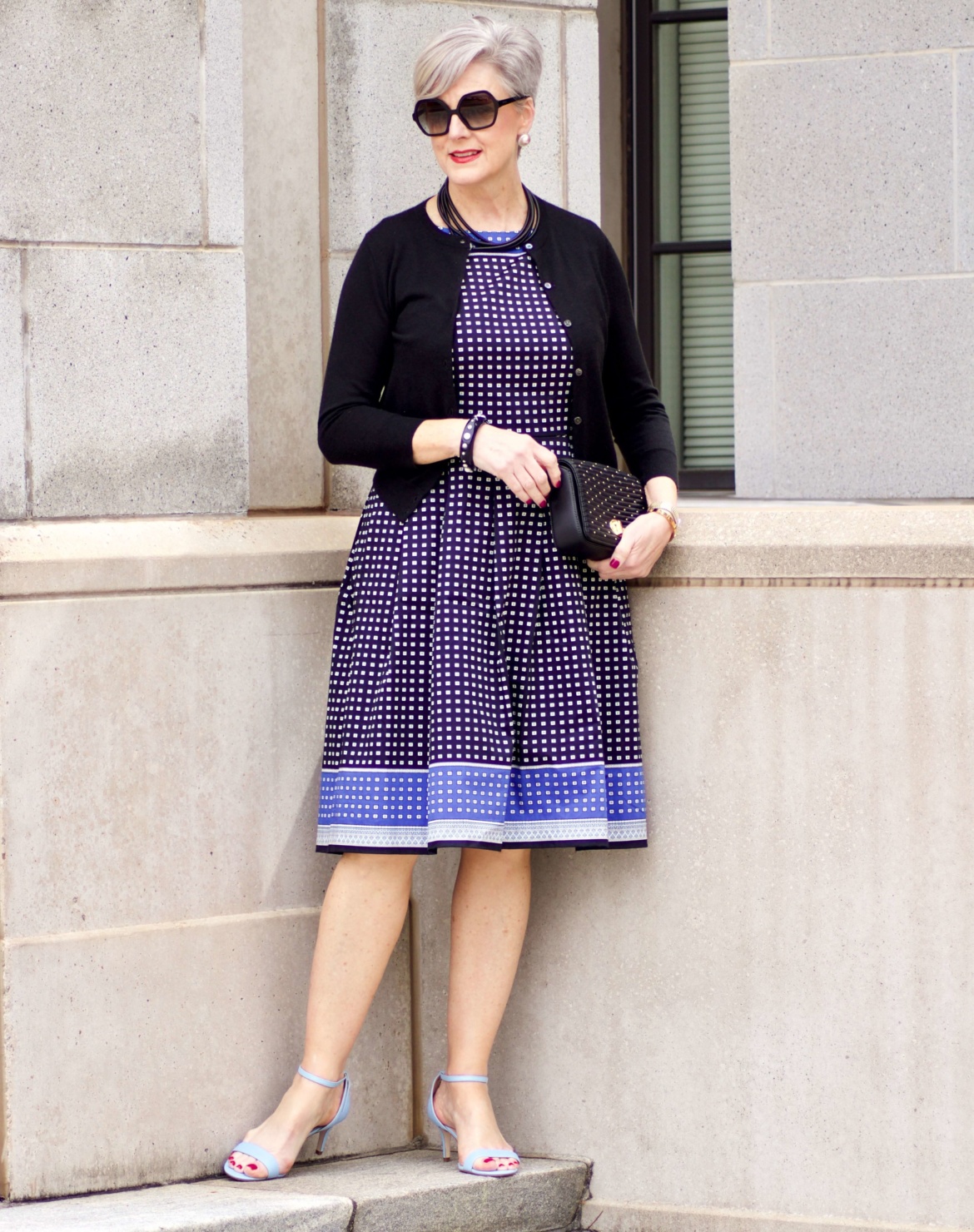 beth from Style at a Certain Age wears a fit and flare dress, kitten heel sandals, and a black clutch handbag