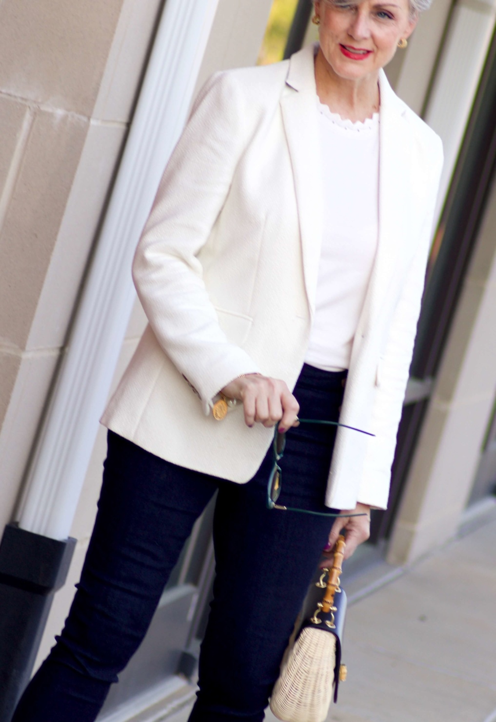 beth from Style at a Certain Age wears a textured ivory blazer, ivory scalloped shell, dark rinse skinny jeans, snakeskin sandals and wicker handbag